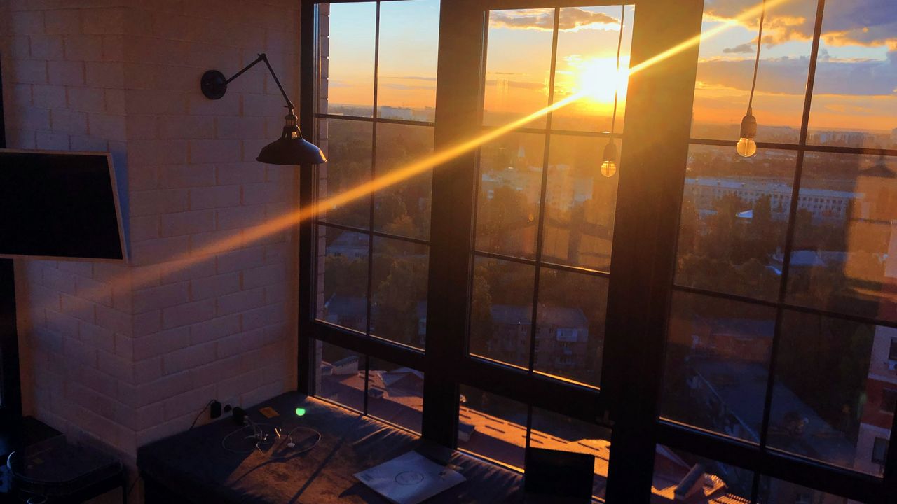Escritorio de oficina con laptop frente a grandes ventanales al atardecer sobre la ciudad