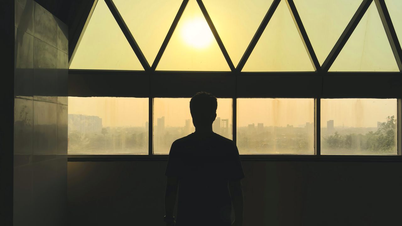 Silueta de una persona junto a un ventanal al atardecer